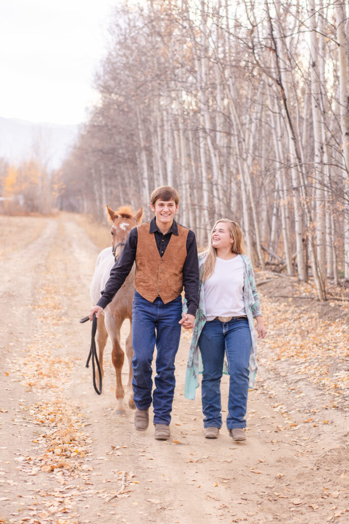 fall western style engagement session. Young couple walking with horse